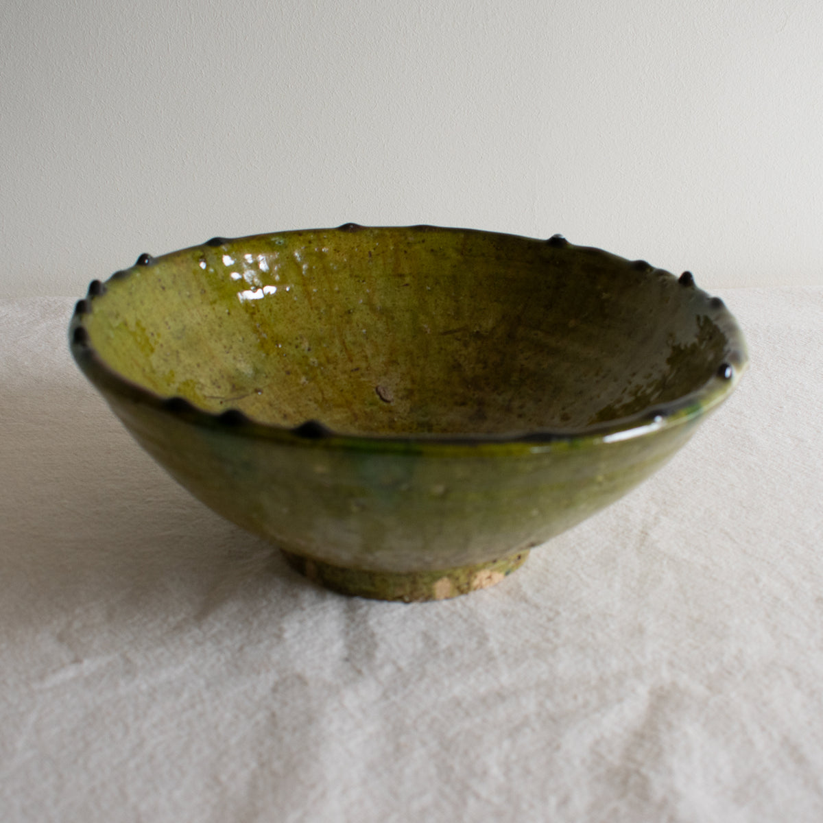 A green ceramic Tamegroute bowl with an irregular rim, placed on a white surface.