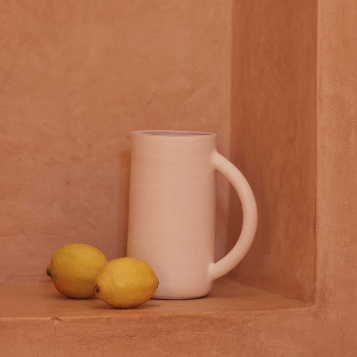White ceramic pitcher with two lemons on a terracotta surface