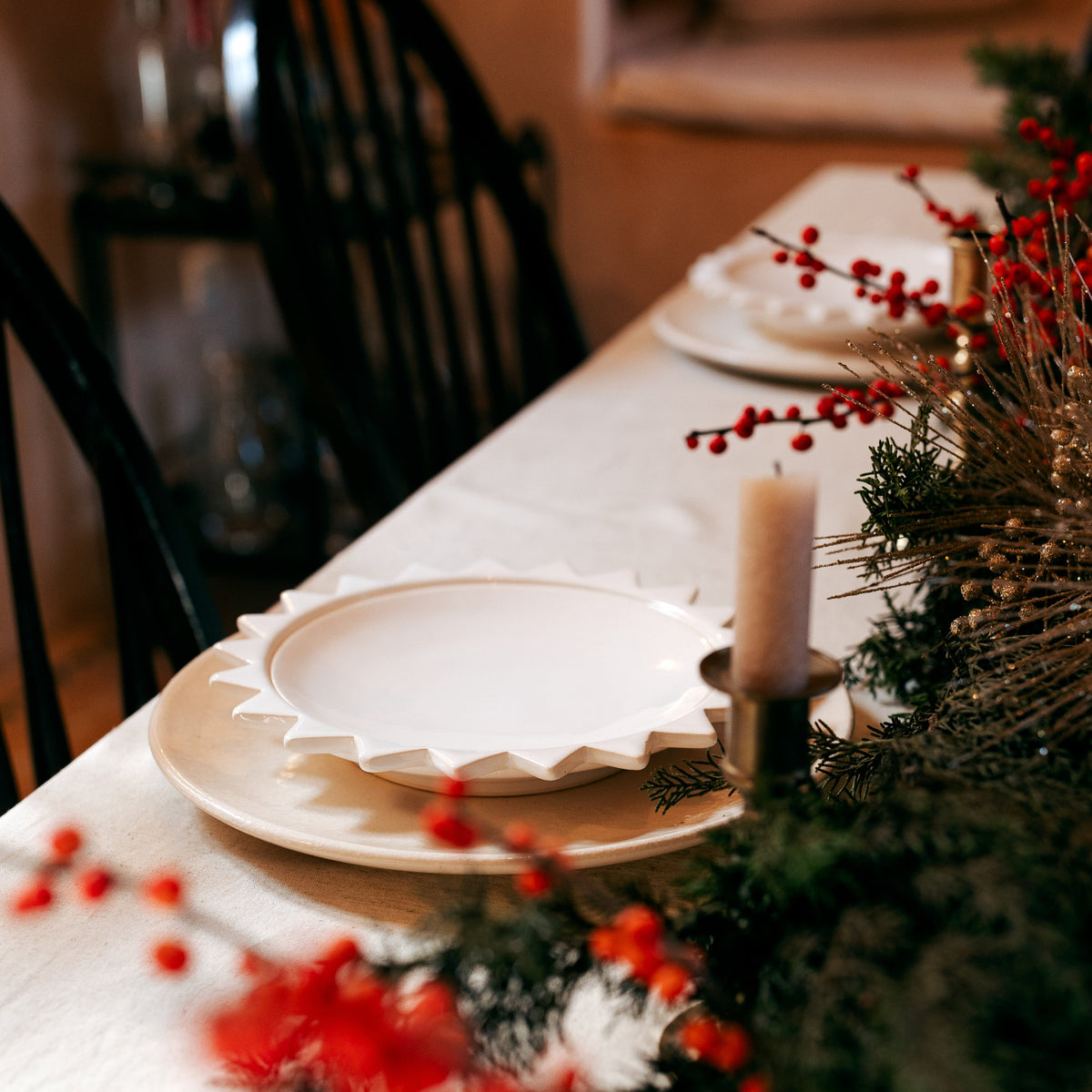 Dining table set with plates, candles, and decorative elements in a warm indoor setting.