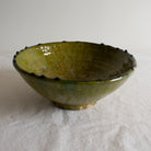 A green ceramic Tamegroute bowl with an irregular rim, placed on a white surface.