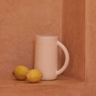 White ceramic pitcher with two lemons on a terracotta surface