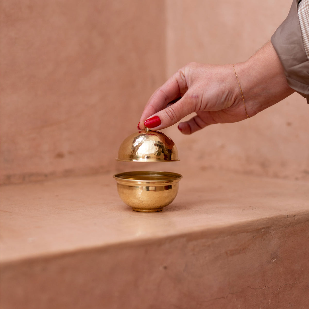 Hand holding a gold decorative object against a beige background