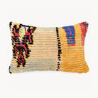 A rectangular decorative throw pillow with a textured, handwoven pattern in mustard yellow, beige, black, red, and blue, shown against a plain white background.