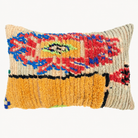 A rectangular handwoven throw pillow with a textured, shaggy surface. The design features a bold abstract pattern in red, blue, yellow, green, and black on a cream-colored base, with a prominent mustard yellow band across the lower half.